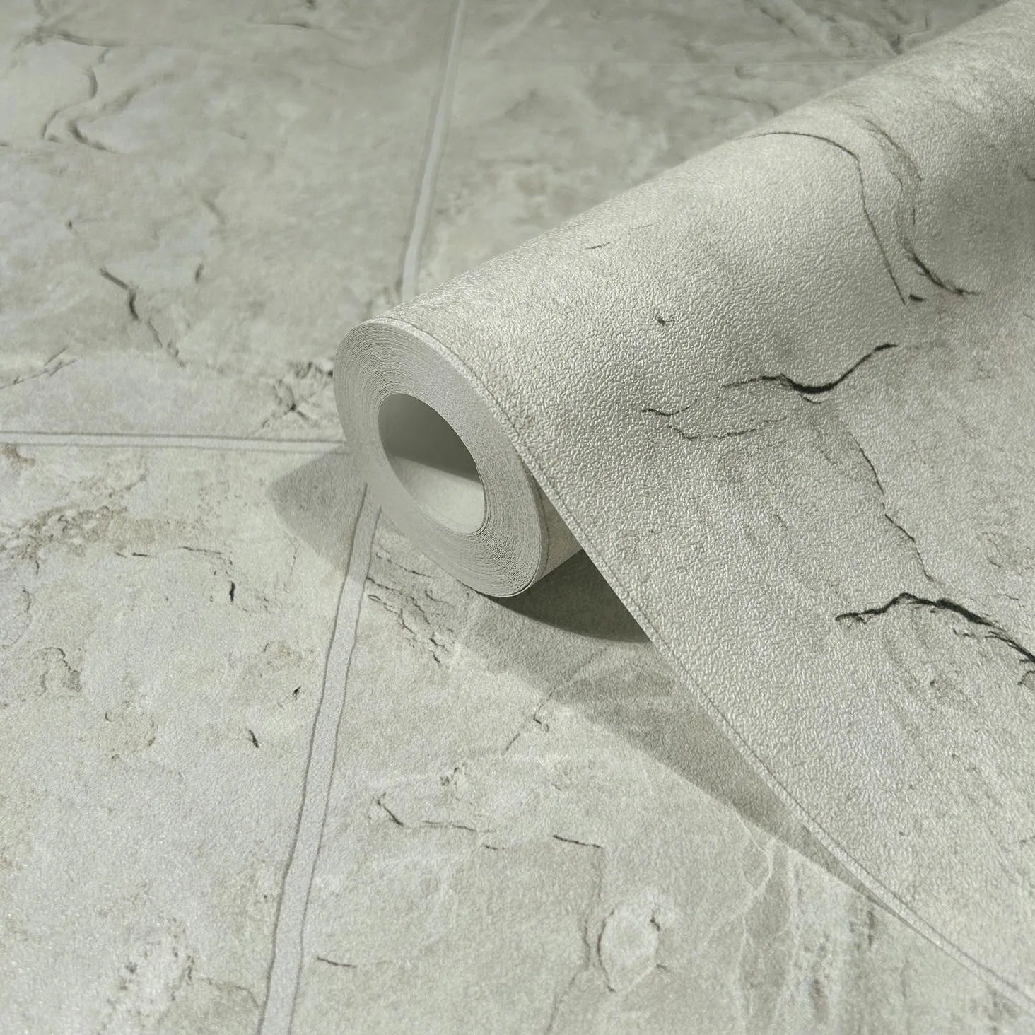 Marburg Struktura 45767 Close-up of a gray stone-look wallpaper roll resting on a matching unrolled sheet, showing subtle veining and faint block seam lines.