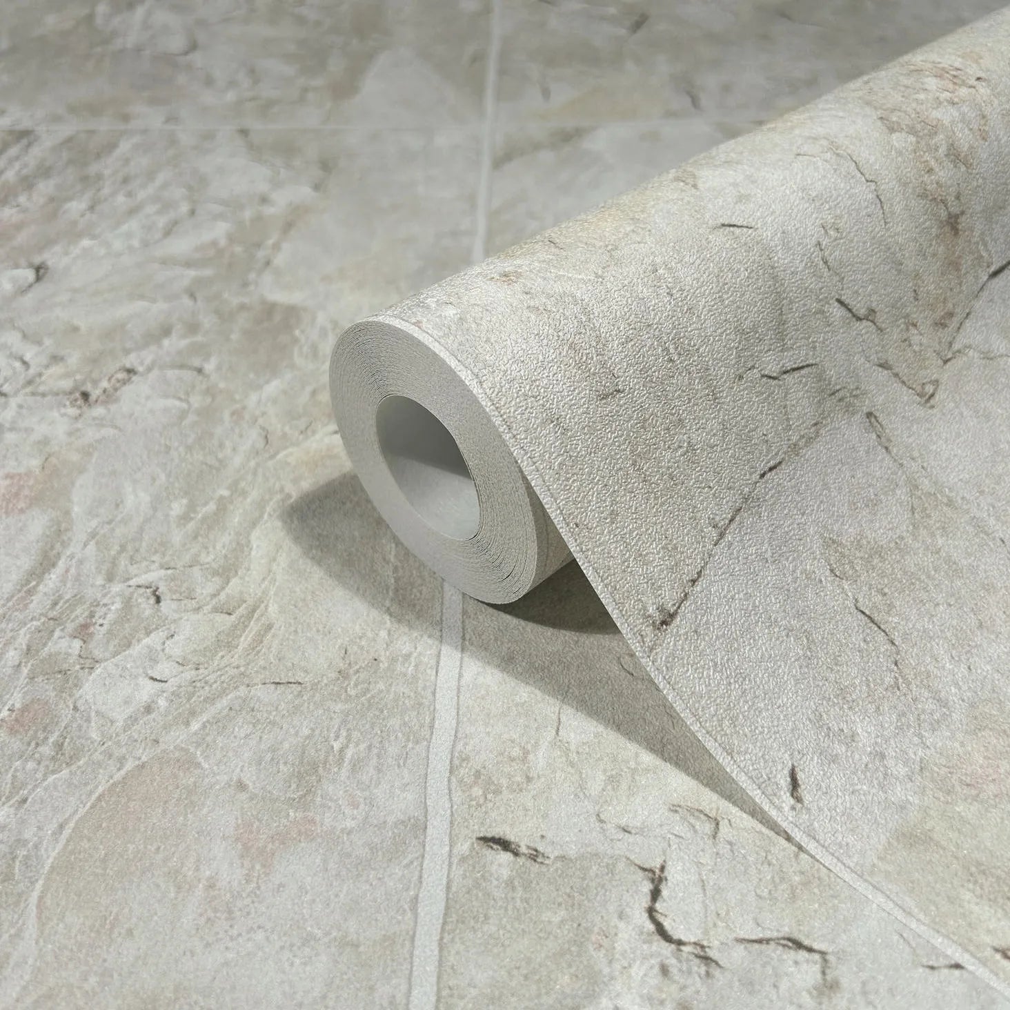 Marburg Struktura 45768 Close-up of a wallpaper roll resting on matching beige stone‑effect wallpaper with subtle veining.