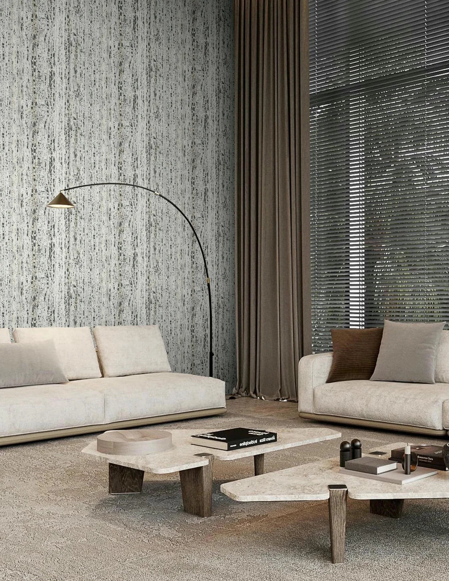 Marburg Travertino 33350 Modern living room featuring a beige and gray vertical striated wallpaper on the feature wall behind two light sofas, with an arc floor lamp, nesting coffee tables with books, tall curtains, and window blinds.