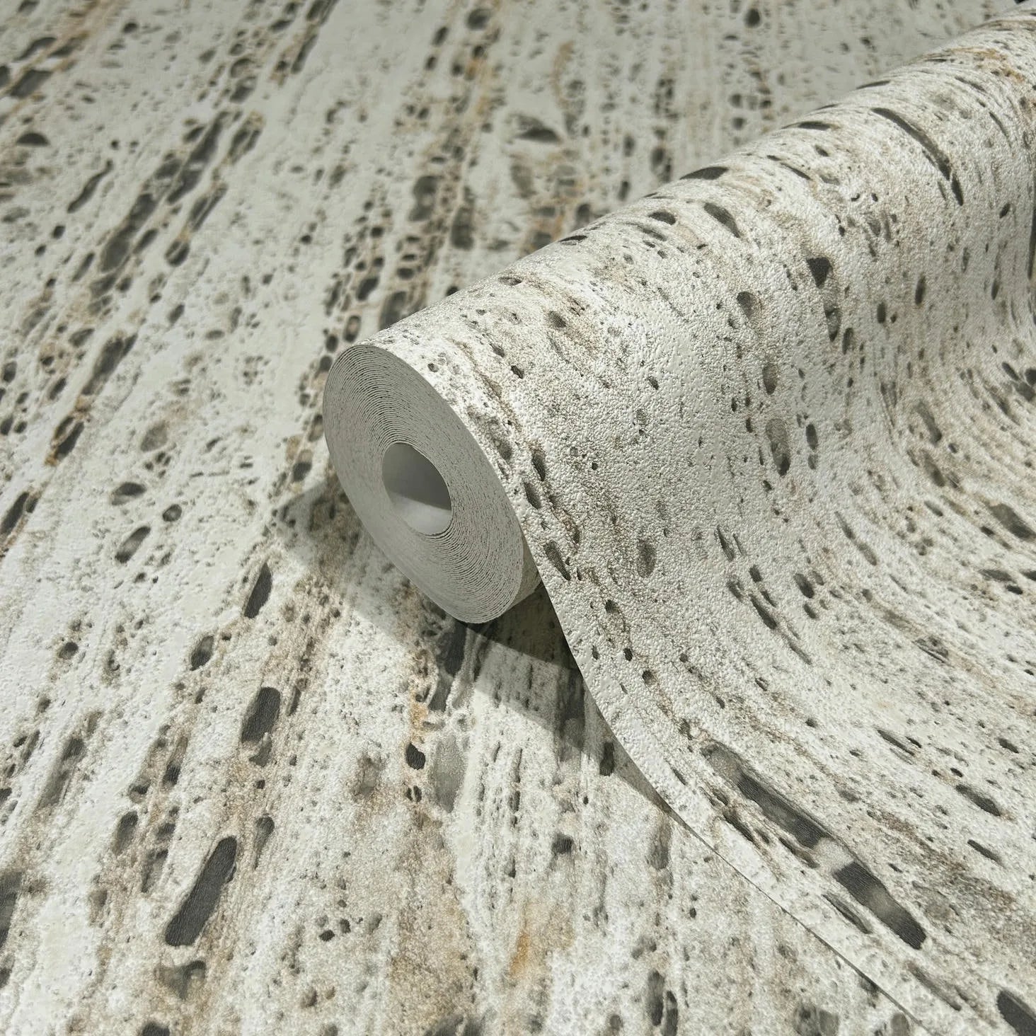 Marburg Travertino 33351 A partially unrolled wallpaper roll showing a beige and gray travertine stone-effect design with porous markings and streaked texture.