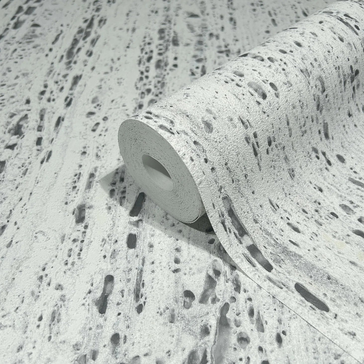 Marburg Travertino 33352 A wallpaper roll partially unrolled on matching material, showing a gray and white travertine stone–look pattern with irregular streaks and pits.