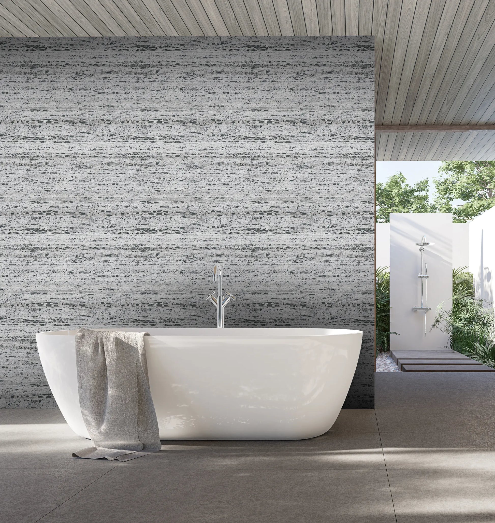Marburg Travertino 33353 Gray horizontal stone-look wallpaper on a feature wall behind a freestanding bathtub with a draped towel; partial view to an outdoor shower and greenery.