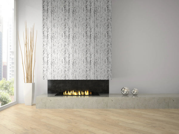 Marburg Travertino 33353 Gray-on-white abstract vertical streak wallpaper covers the chimney breast above a modern linear fireplace on a concrete hearth, with a tall white planter holding sticks and two metallic decorative spheres nearby.