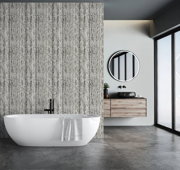 Marburg Travertino 33354 Gray vertical striated wallpaper on a feature wall behind a freestanding bathtub in a modern bathroom with a floating wood vanity, round mirror, and large windows.