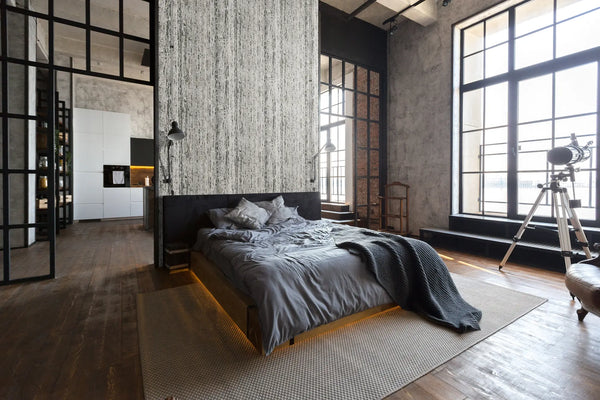 Marburg Travertino 33354 Industrial-style bedroom featuring a vertical gray-and-white streaked wallpaper on the wall behind the bed, with large grid windows, wall-mounted lamps, and a telescope on a tripod in view.