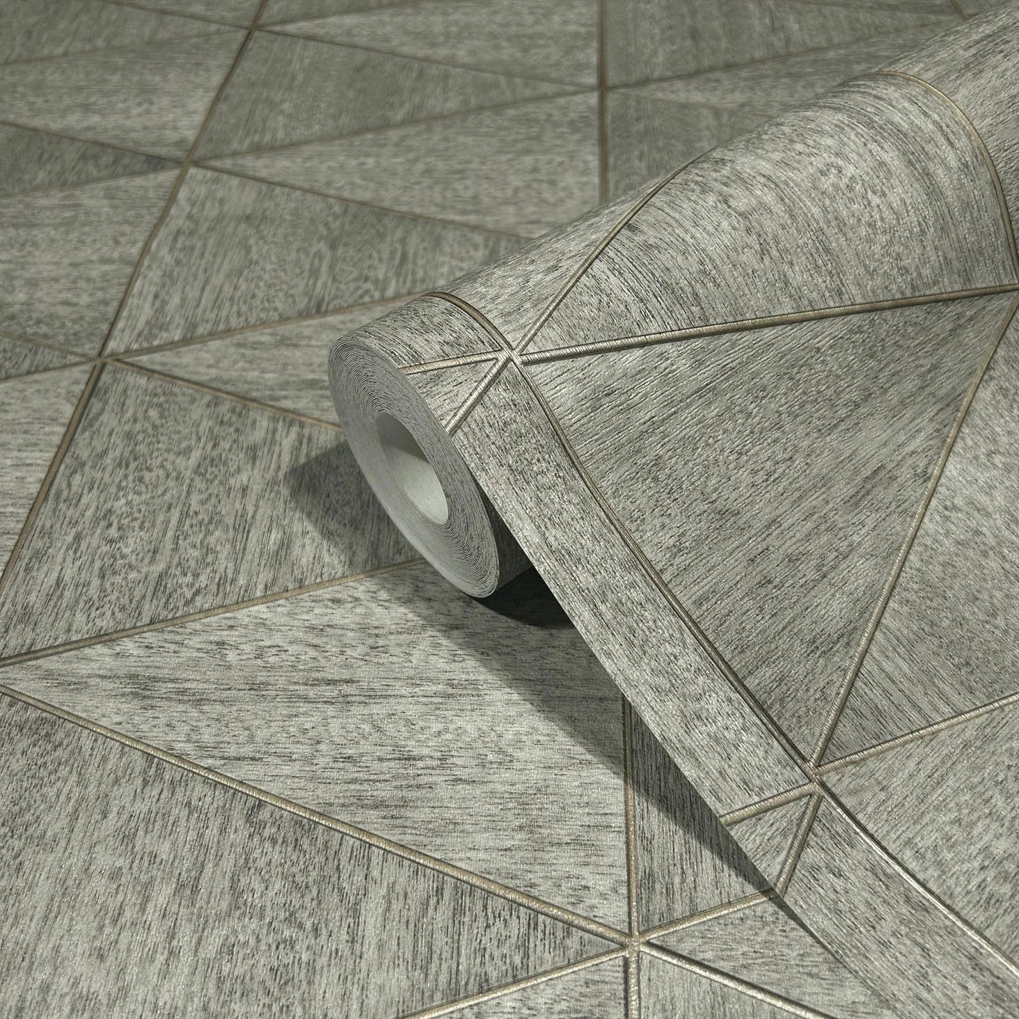 Marburg Travertino 33355 Close-up of a gray geometric wallpaper roll with thin diagonal lines forming triangles, resting on the same patterned surface.