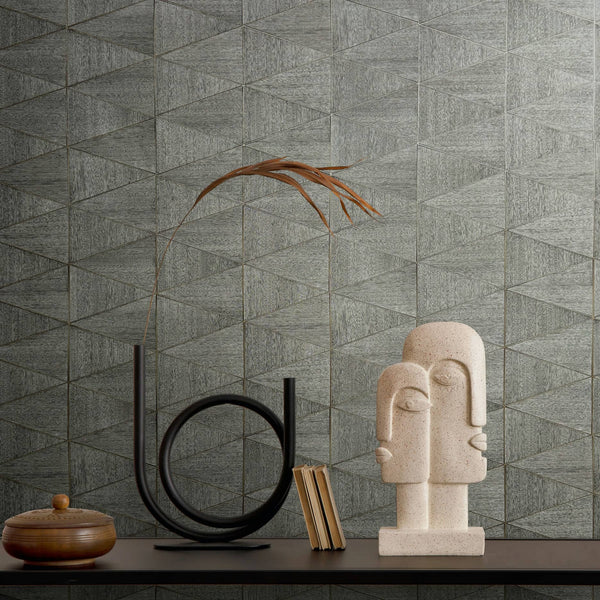 Marburg Travertino 33355 Gray geometric triangle wallpaper shown behind a console with a black circular sculpture holding a dried stem, an abstract stone bust, a few books, and a small lidded wooden bowl.