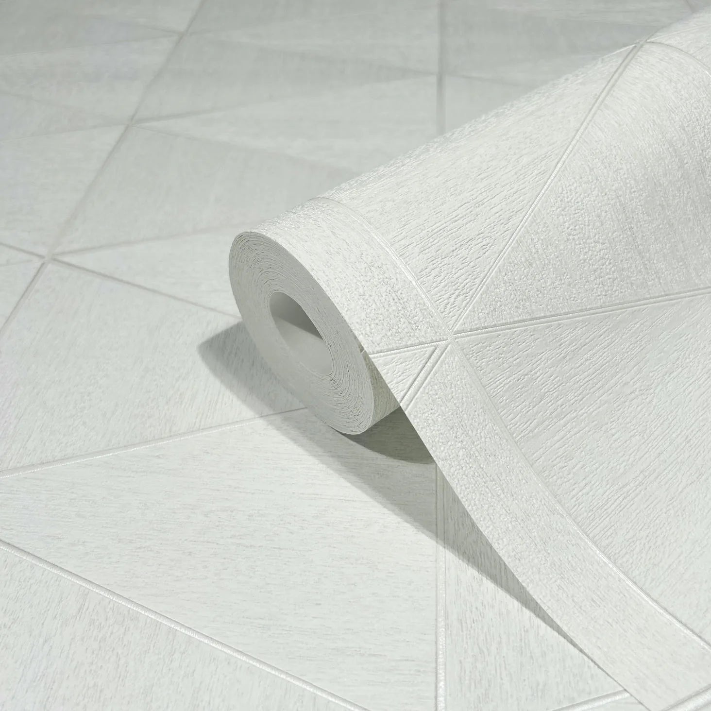 Marburg Travertino 33356 Close-up of a white textured wallpaper roll resting on matching wallpaper with large triangular shapes and raised lines.