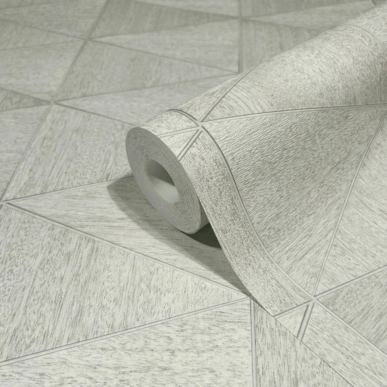 Marburg Travertino 33357 Close-up of a wallpaper roll resting on matching wallpaper with a light gray-beige geometric triangle pattern and subtle textured look.