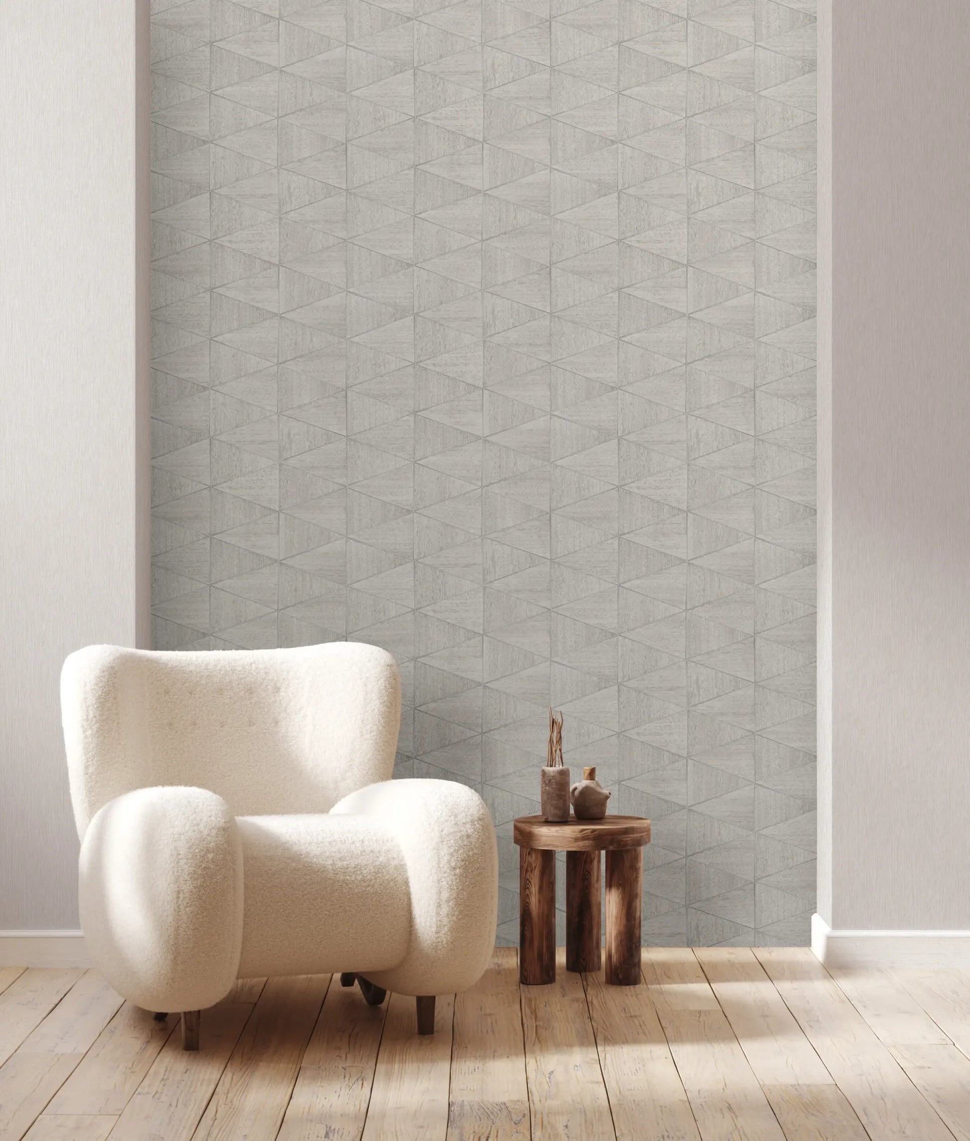 Marburg Travertino 33357 Gray geometric triangle wallpaper on a feature wall behind a plush white armchair and a small wooden side table on light wood flooring.