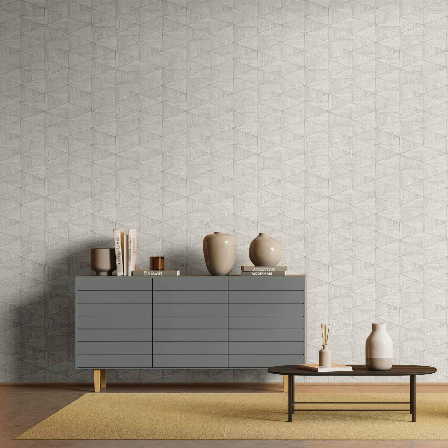 Marburg Travertino 33357 Beige and gray geometric triangle wallpaper behind a gray sideboard with books and ceramic vases, next to a low oval coffee table with a vase and reed diffuser on a rug.