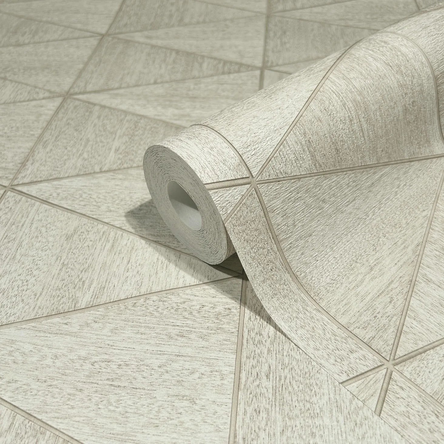 Marburg Travertino 33358 A wallpaper roll resting on matching wallpaper showing a light beige geometric pattern of intersecting lines with a subtle woodgrain texture.