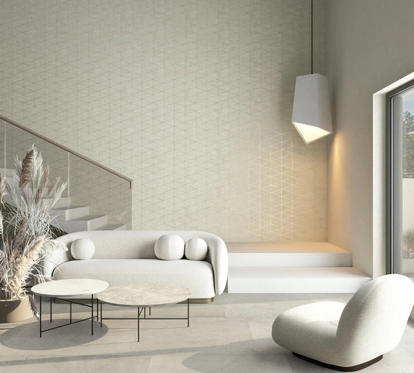 Marburg Travertino 33358 Beige geometric triangle-patterned wallpaper shown in a modern living room with a white sofa, lounge chair, nesting coffee tables, a glass-railed staircase, a pendant light, a few steps, and a large window.
