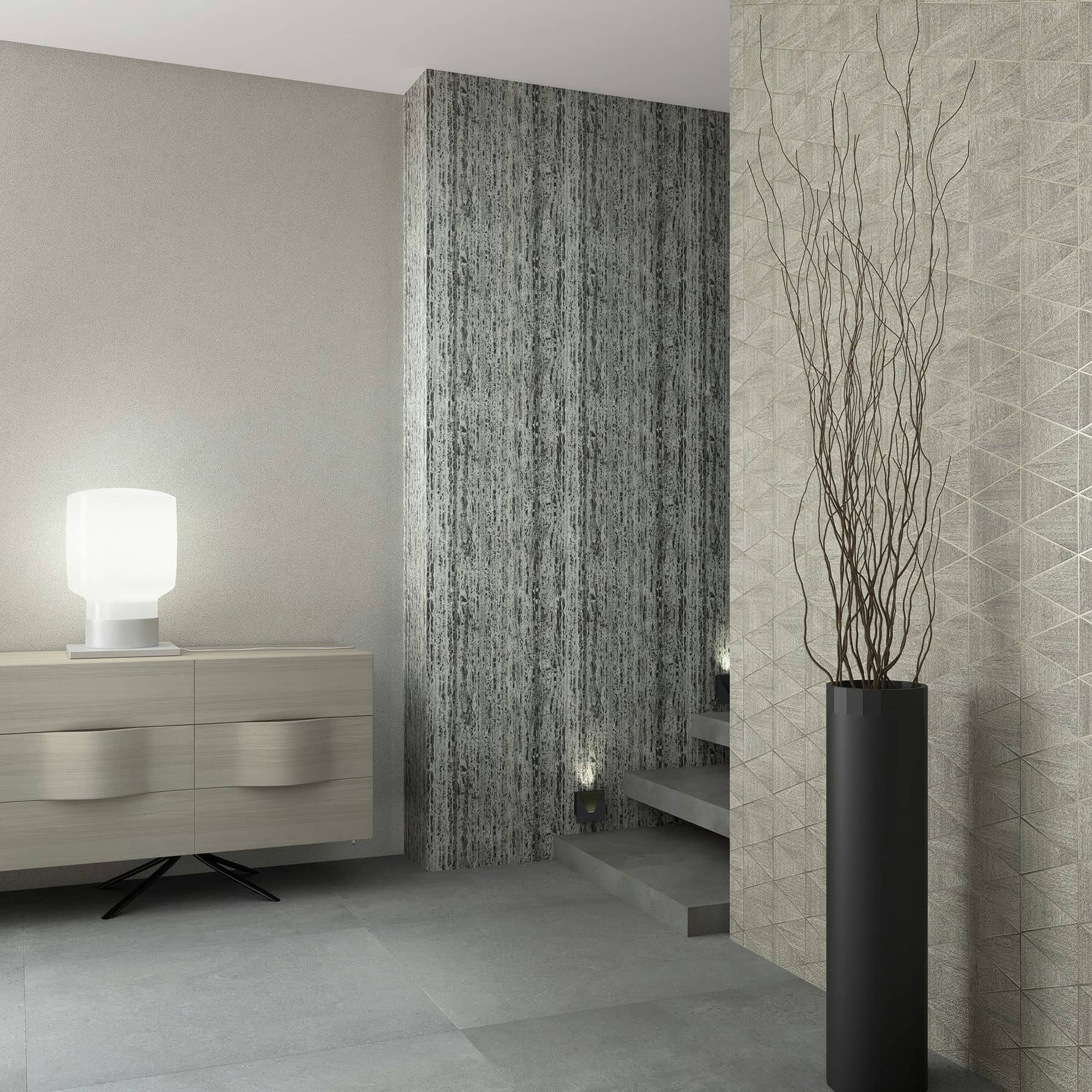 Marburg Travertino 33358 Staircase area with three coordinating wallpapers: a light beige textured wall on the left, a dark vertically striated accent on the central column, and a beige geometric triangle pattern on the right. A light wood sideboard with a white table lamp sits to the.