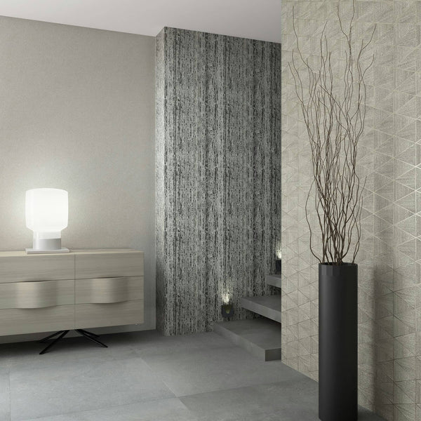 Marburg Travertino 33358 Staircase area with three coordinating wallpapers: a light beige textured wall on the left, a dark vertically striated accent on the central column, and a beige geometric triangle pattern on the right. A light wood sideboard with a white table lamp sits to the.