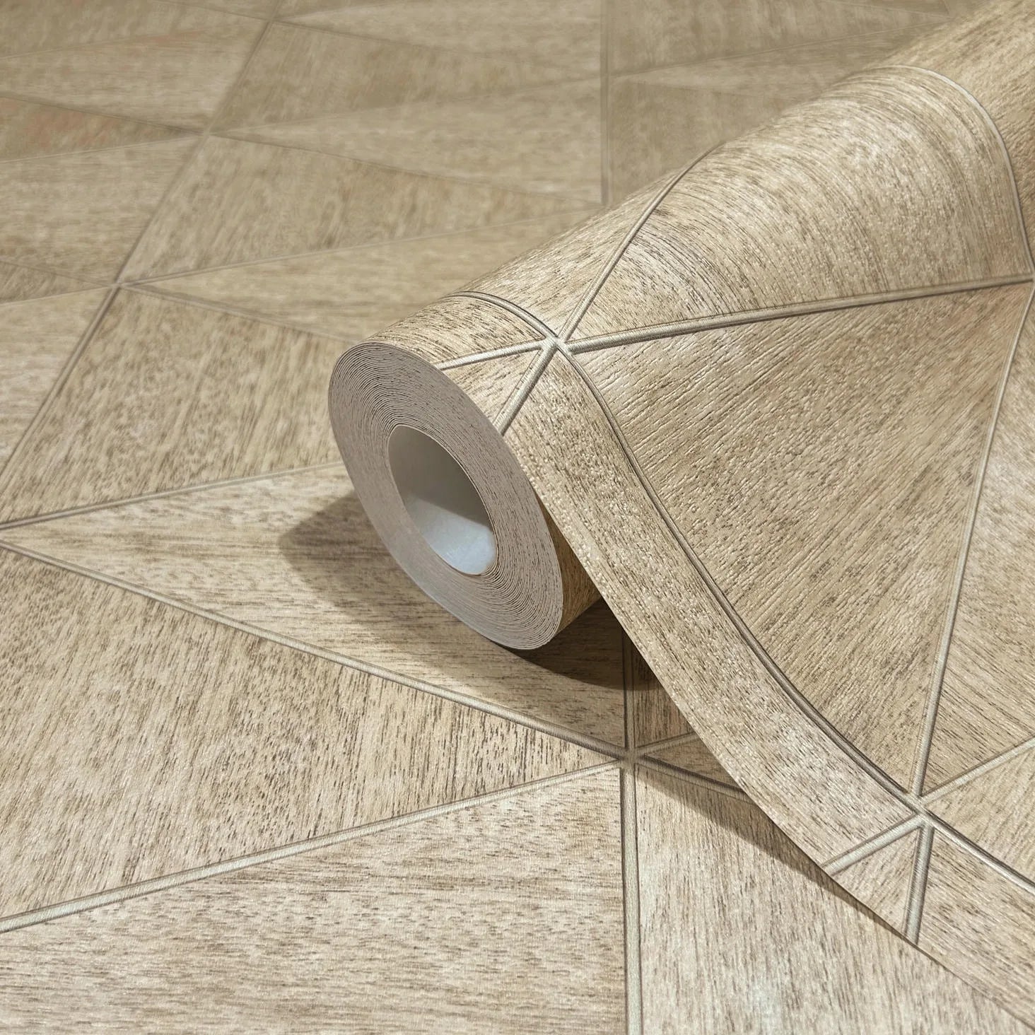 Marburg Travertino 33359 Wallpaper roll in beige and brown with a wood-textured geometric pattern of intersecting lines forming triangles, shown partially unrolled on a matching surface.
