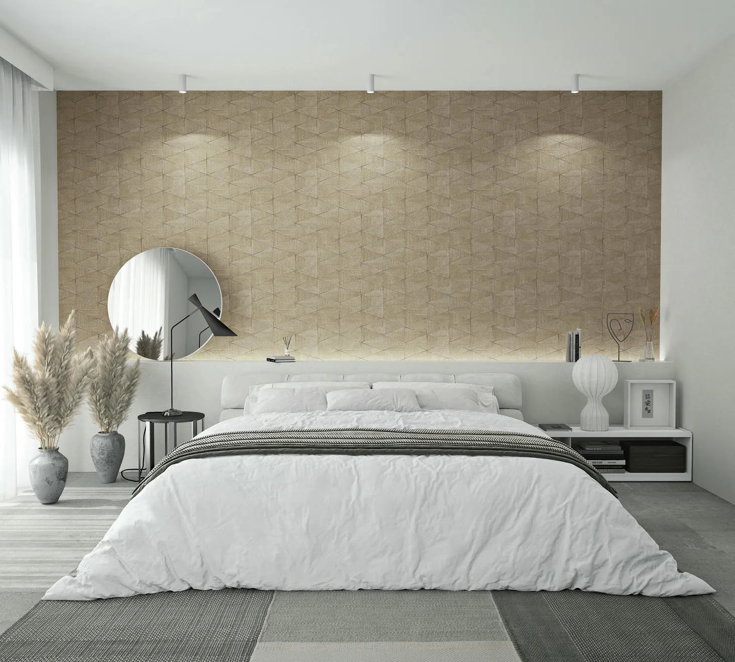 Marburg Travertino 33359 Bedroom scene featuring a beige geometric textured wallpaper feature wall behind a low bed with white bedding, a round mirror and black side table with lamp on the left, floor vases with pampas grass, and a white nightstand with a ribbed lamp on the right.
