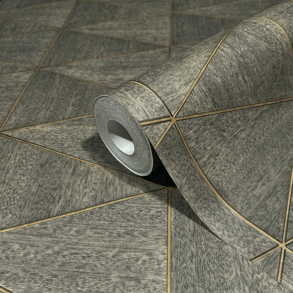 Marburg Travertino 33360 A wallpaper roll resting on the same pattern, showing a textured brown-gray surface crossed by thin gold-toned lines that create large triangular shapes.