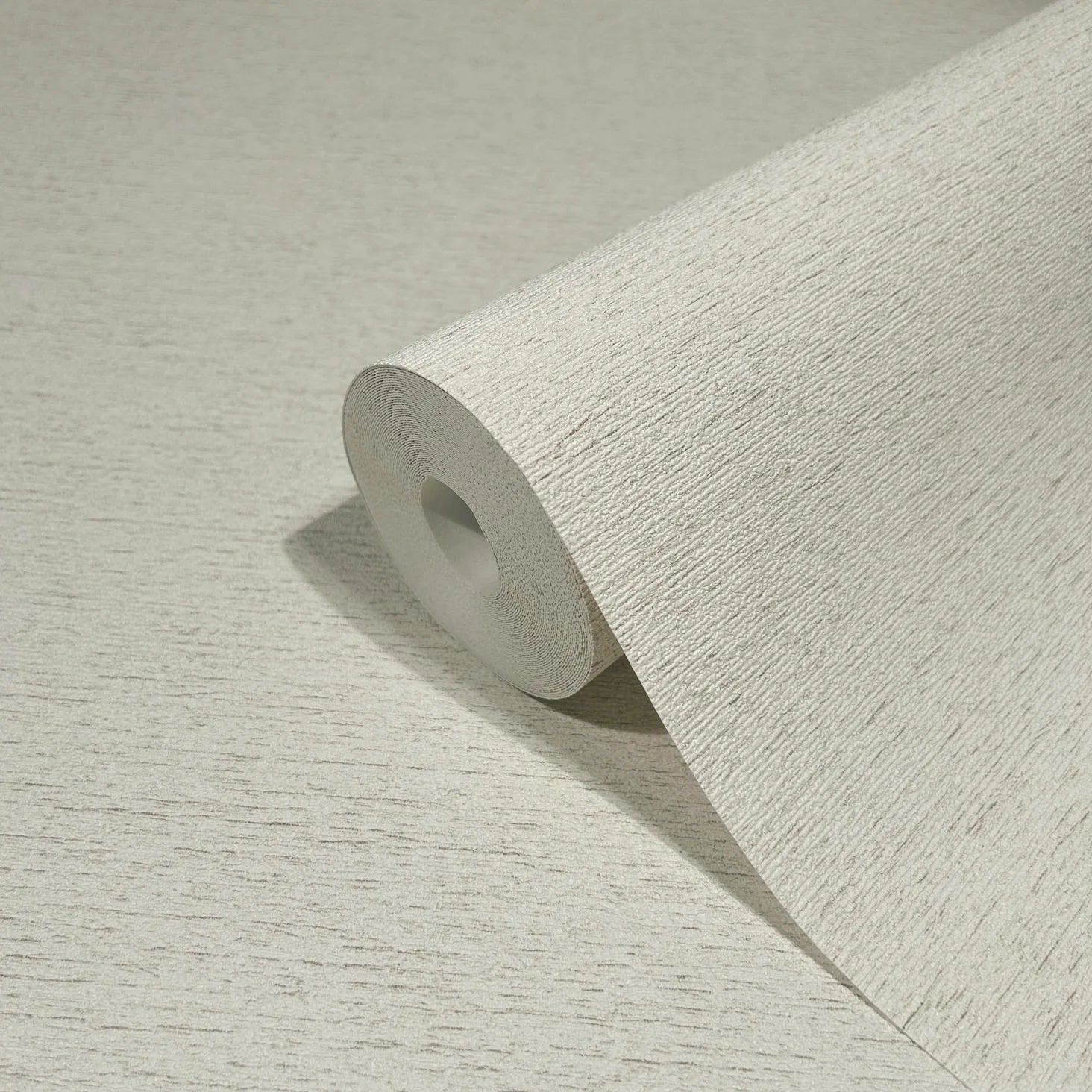 Marburg Travertino 33367 Close-up of a light beige textured wallpaper roll on a matching surface, showing fine horizontal striations.