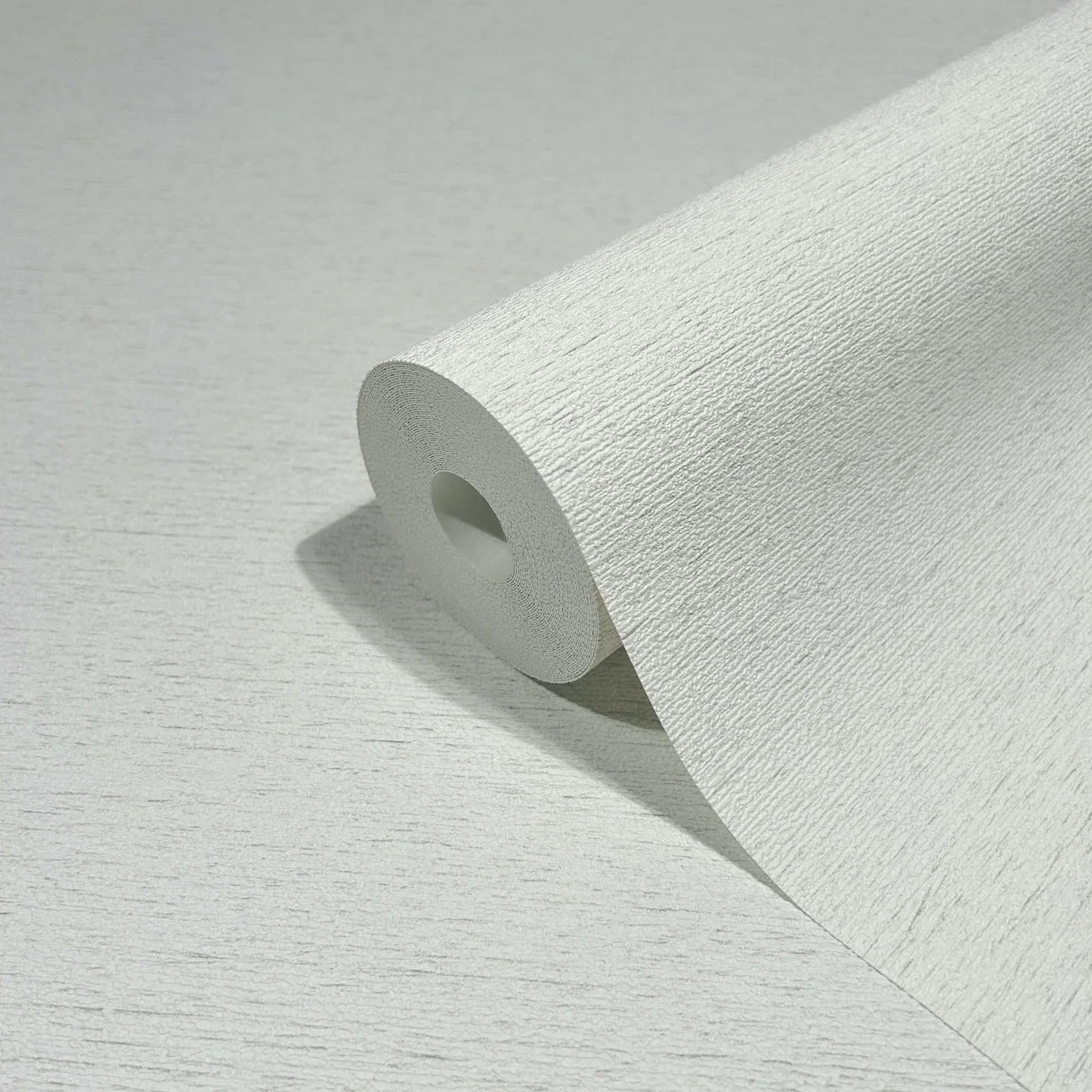Marburg Travertino 33368 Close-up product shot of a white wallpaper roll showing a fine horizontal striated texture, resting on the same wallpaper.