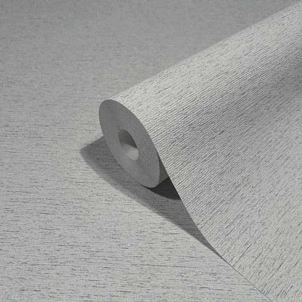 Marburg Travertino 33370 Close-up of a gray textured wallpaper roll, partially unrolled on the same surface, showing fine horizontal striations.
