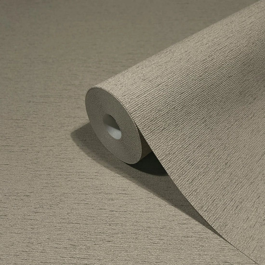 Marburg Travertino 33371 Brown textured wallpaper with fine horizontal lines behind a dark console styled with a tall rectangular vase of grasses, two white ceramic vases with dried stems, and a stack of magazines topped with a small candle.