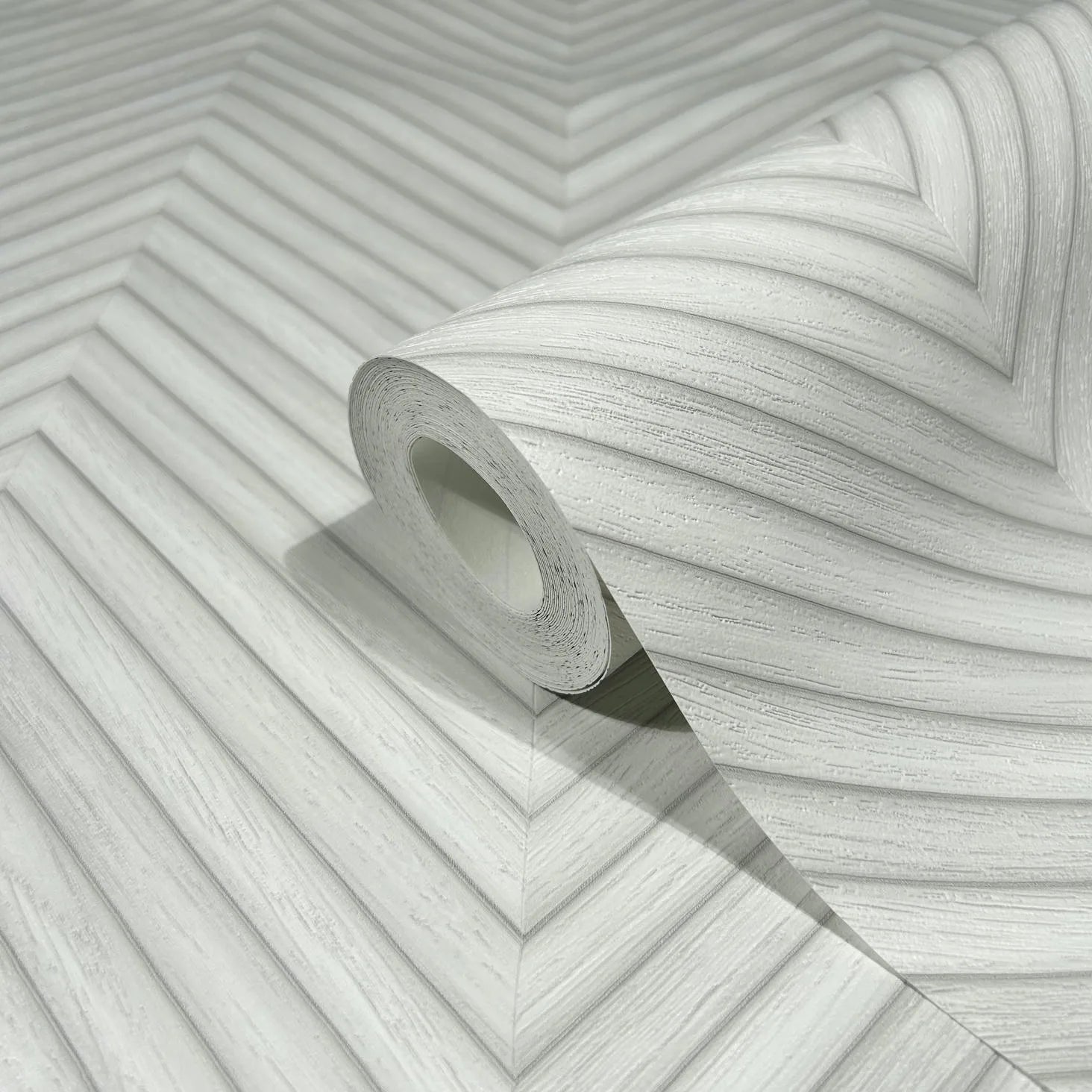 Marburg Travertino 33375 Close-up of a wallpaper roll resting on matching wallpaper showing a light gray and white chevron pattern with fine linear texture.