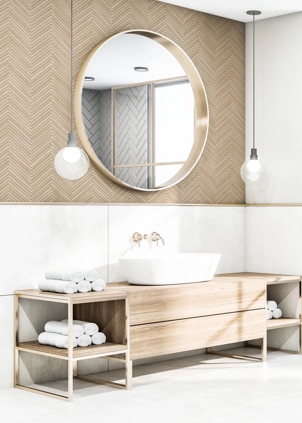 Marburg Travertino 33376 Beige chevron-pattern wallpaper on the upper wall behind a bathroom vanity with a round mirror, two pendant lights, a white basin sink with wall-mounted faucet, and rolled towels above white wall tiles.
