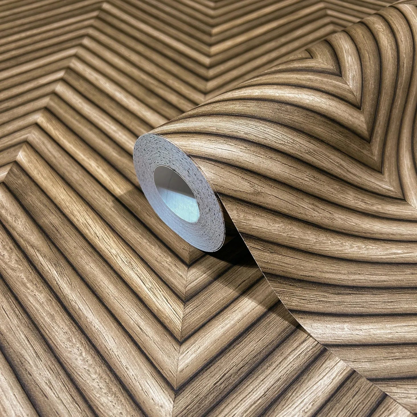 Marburg Travertino 33377 Close-up of a wallpaper roll resting on matching wallpaper with a brown woodgrain-effect chevron design.
