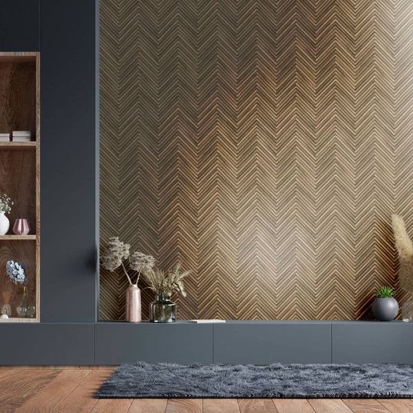 Marburg Travertino 33377 Room scene showing brown chevron herringbone wallpaper behind a low gray cabinet, with dried stems in vases, a small potted plant, open shelving at left, and a gray rug on a wood floor.