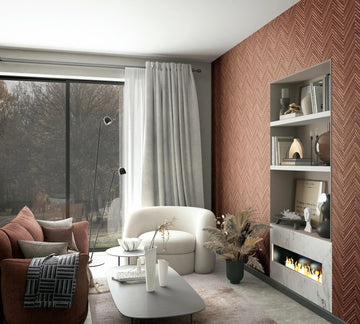 Marburg Travertino 33379 Reddish-brown chevron wallpaper used as a feature wall in a living room with built-in shelves and a linear fireplace, beside a large window with curtains, a sofa, an armchair, a coffee table, and a floor lamp.