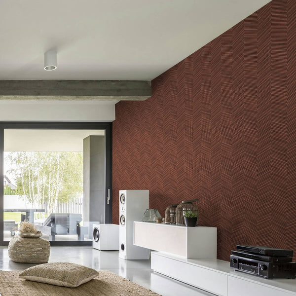 Marburg Travertino 33379 Living room scene showing a brown-red chevron wallpaper used on a feature wall beside a low white media console, speakers, plants, and a large sliding glass door.