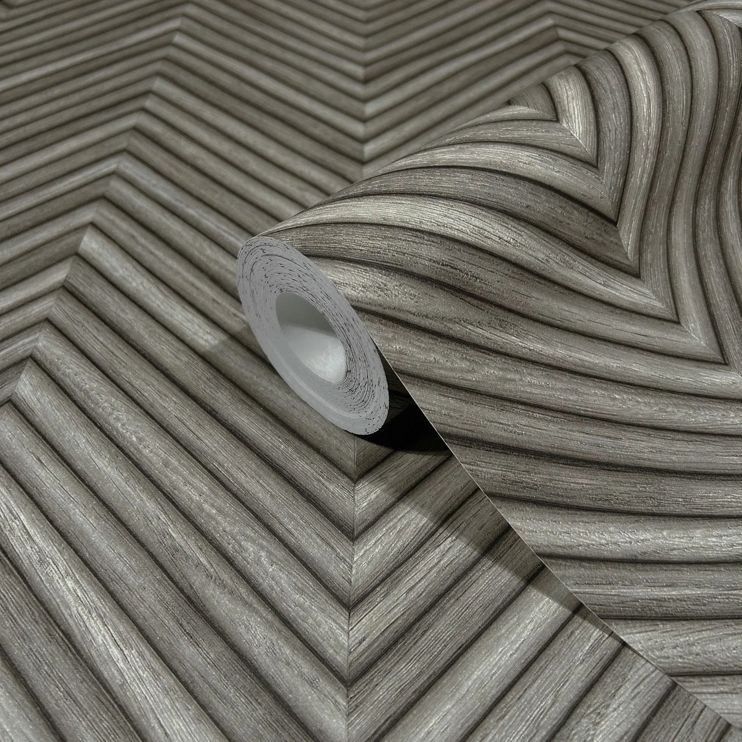 Marburg Travertino 33380 A gray wallpaper roll on a matching unrolled sheet showing a dimensional chevron pattern with woodgrain-like striations.