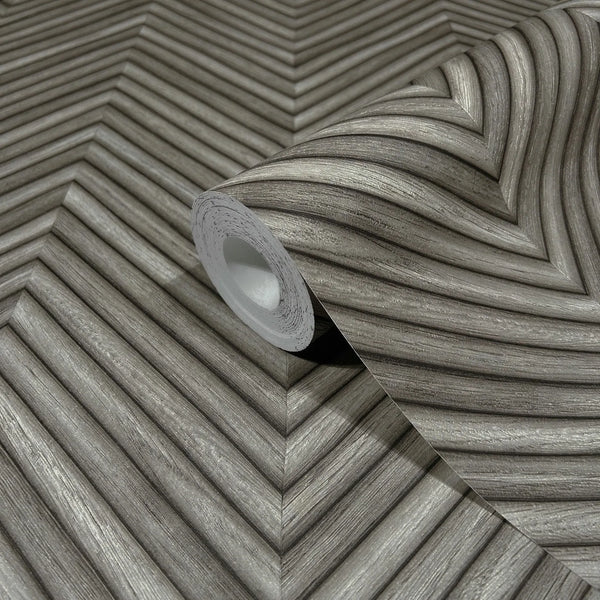Marburg Travertino 33380 A gray wallpaper roll on a matching unrolled sheet showing a dimensional chevron pattern with woodgrain-like striations.