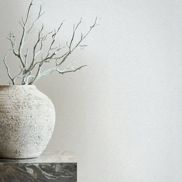 Marburg Travertino 33381 Light gray textured wallpaper with a fine wavy pattern; a rough ceramic vase with bare branches sits on a stone pedestal in front.