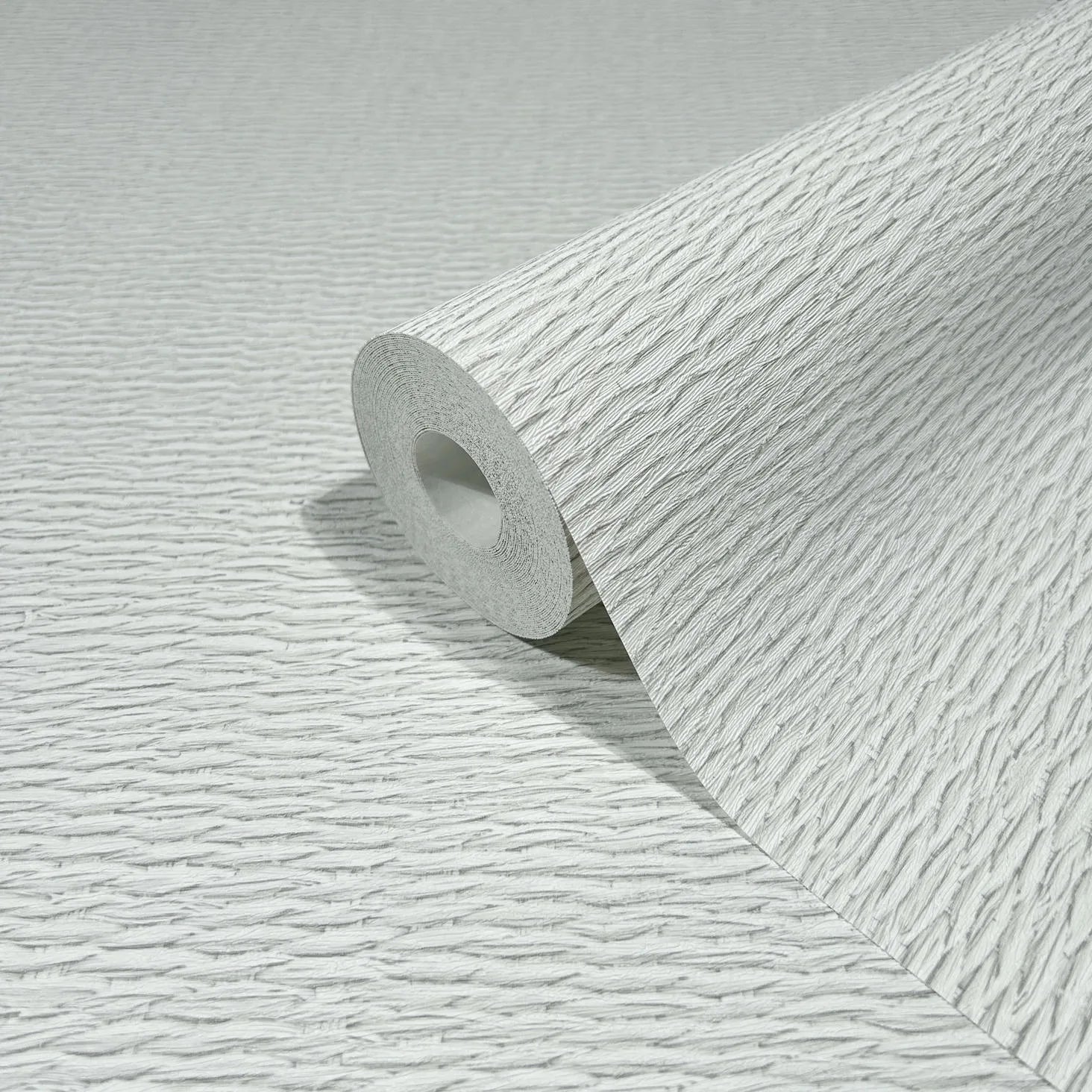 Marburg Travertino 33381 Close-up of a light gray and white textured wallpaper roll with irregular horizontal ridges, resting on the same pattern surface.