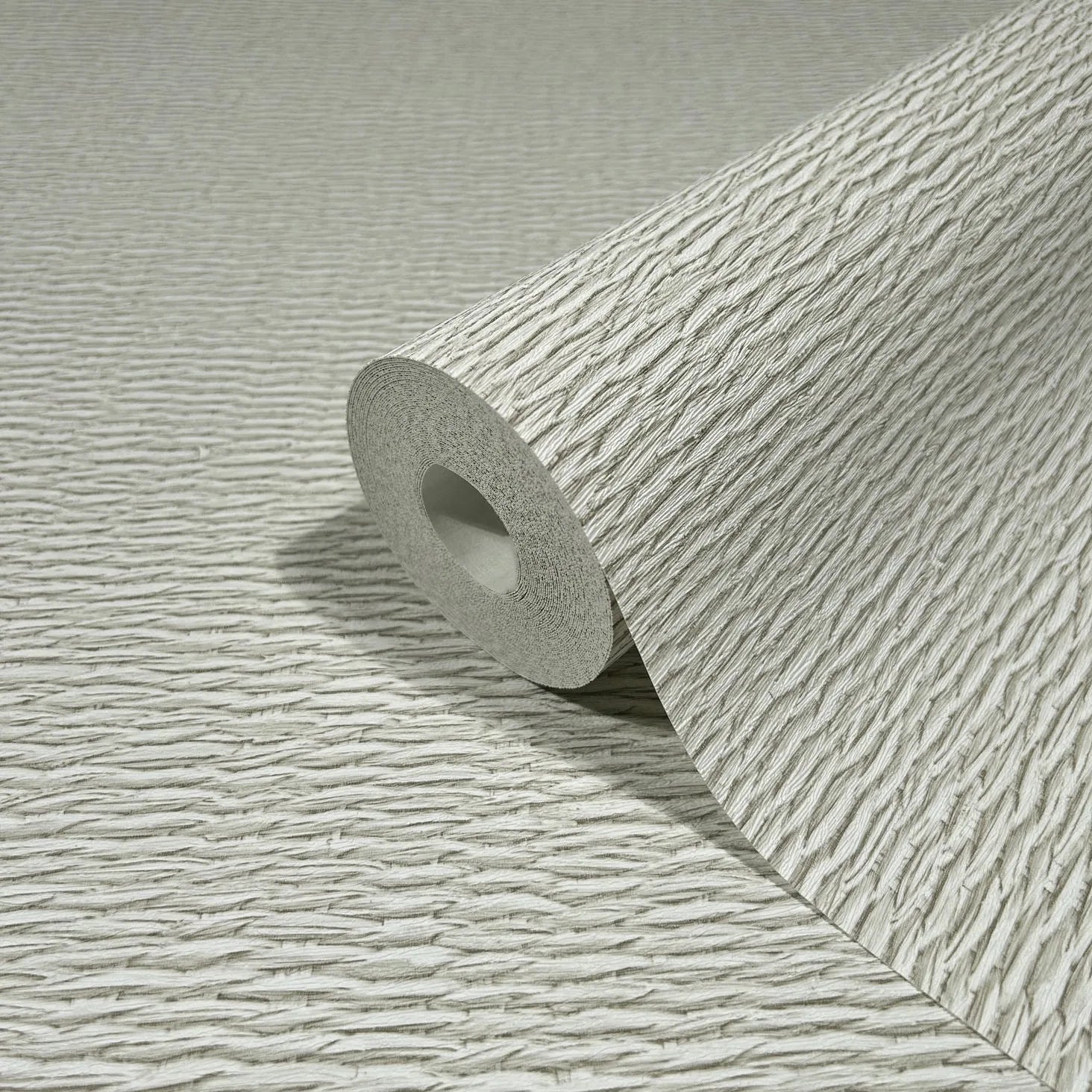Marburg Travertino 33382 Close-up of a wallpaper roll with raised, wavy linear texture in light beige, resting on a matching unrolled sheet.