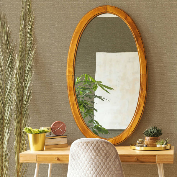 Marburg Travertino 33384 Textured beige wallpaper with subtle horizontal lines behind a wooden desk scene featuring an oval wood-framed mirror, upholstered chair, potted plants, a small clock, books, and a tray.