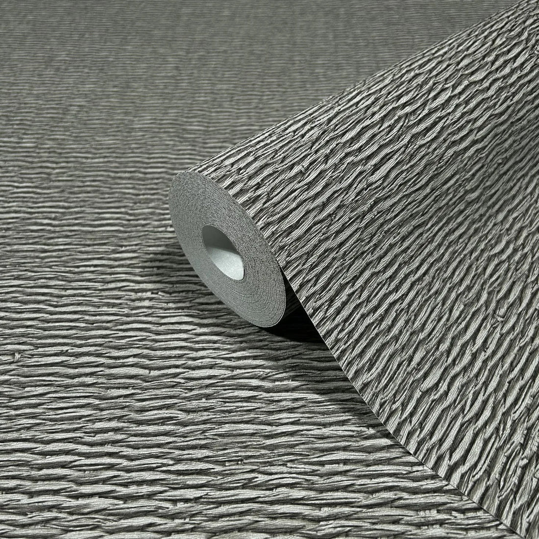 Marburg Travertino 33386 Gray textured wallpaper with horizontal ripple lines shown above a light stone countertop and backsplash, with ceramic bowls, a small vase with dried stems, a dark plate, a woven placemat, and wood cabinets below.