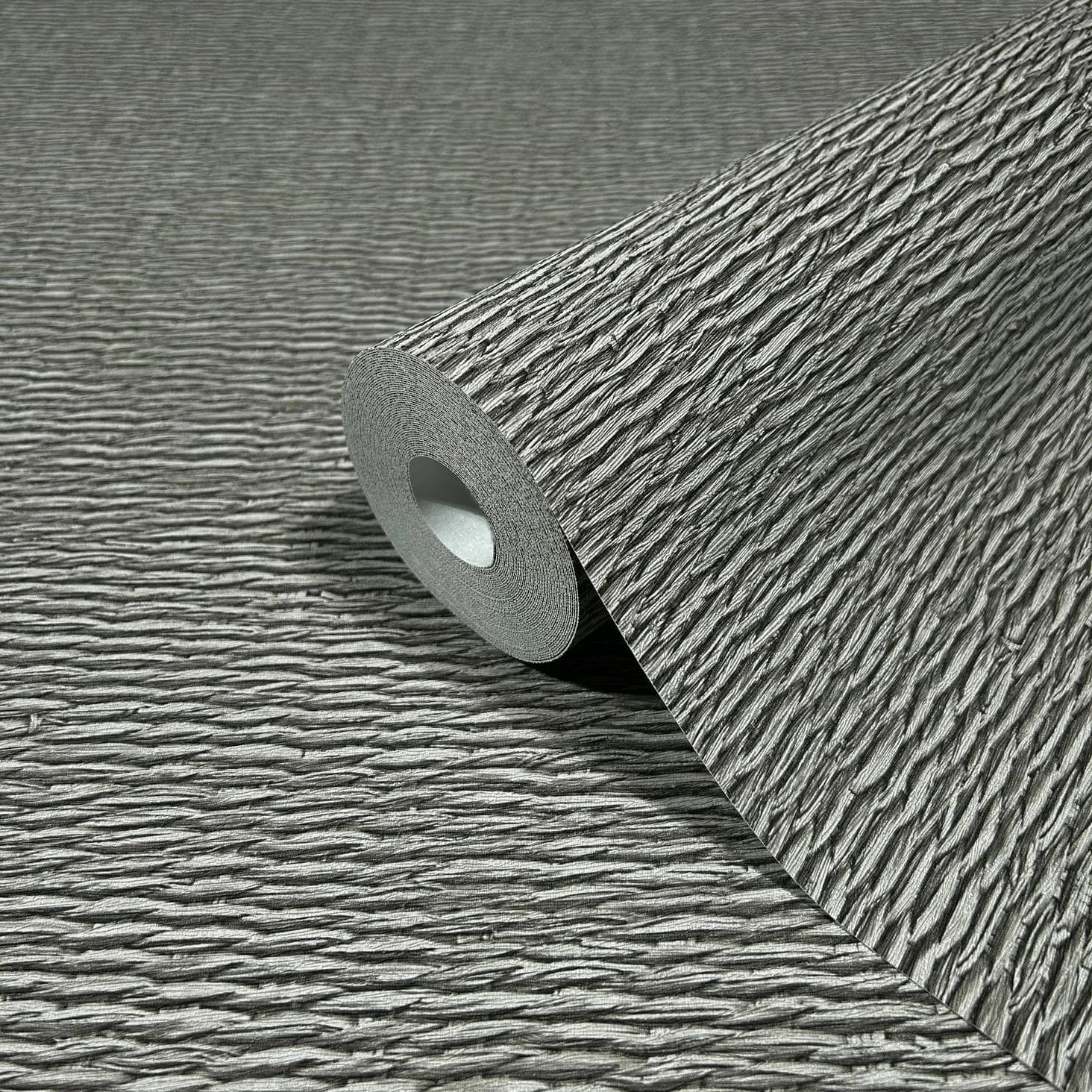 Marburg Travertino 33386 Close-up of a gray wallpaper roll with raised horizontal ridges, resting on the same textured pattern.
