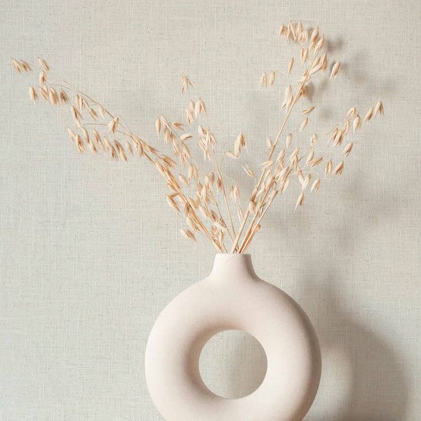Marburg Travertino 33389 Light beige linen-look textured wallpaper with a fine crosshatch pattern, shown behind a round ring ceramic vase holding dried stems.