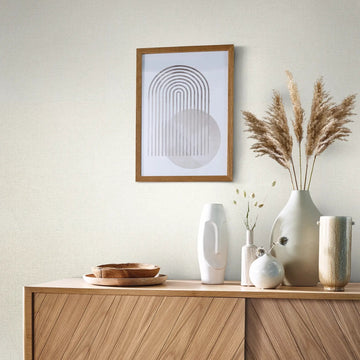 Marburg Travertino 33389 Light beige textured wallpaper behind a wooden sideboard topped with decorative vases, dried grasses, and wooden bowls, with a framed abstract print on the wall.