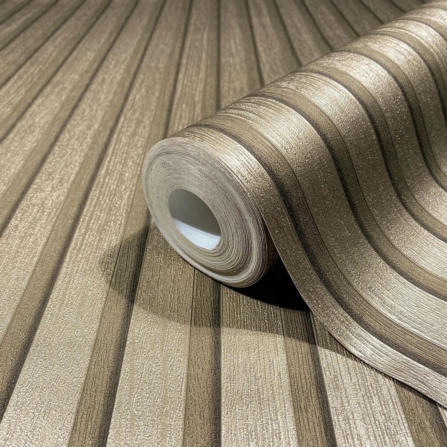 Marburg Travertino 33396 Close-up of a wallpaper roll resting on matching unrolled wallpaper, showing textured metallic gold stripes in alternating widths.
