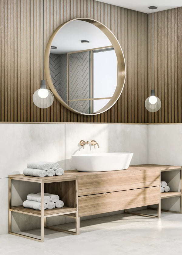 Marburg Travertino 33396 Bathroom scene showing vertical fluted gold wallpaper on the upper wall, a round mirror, two pendant lights, a wood vanity with a white vessel sink and wall-mounted faucet, and rolled towels on open shelves.