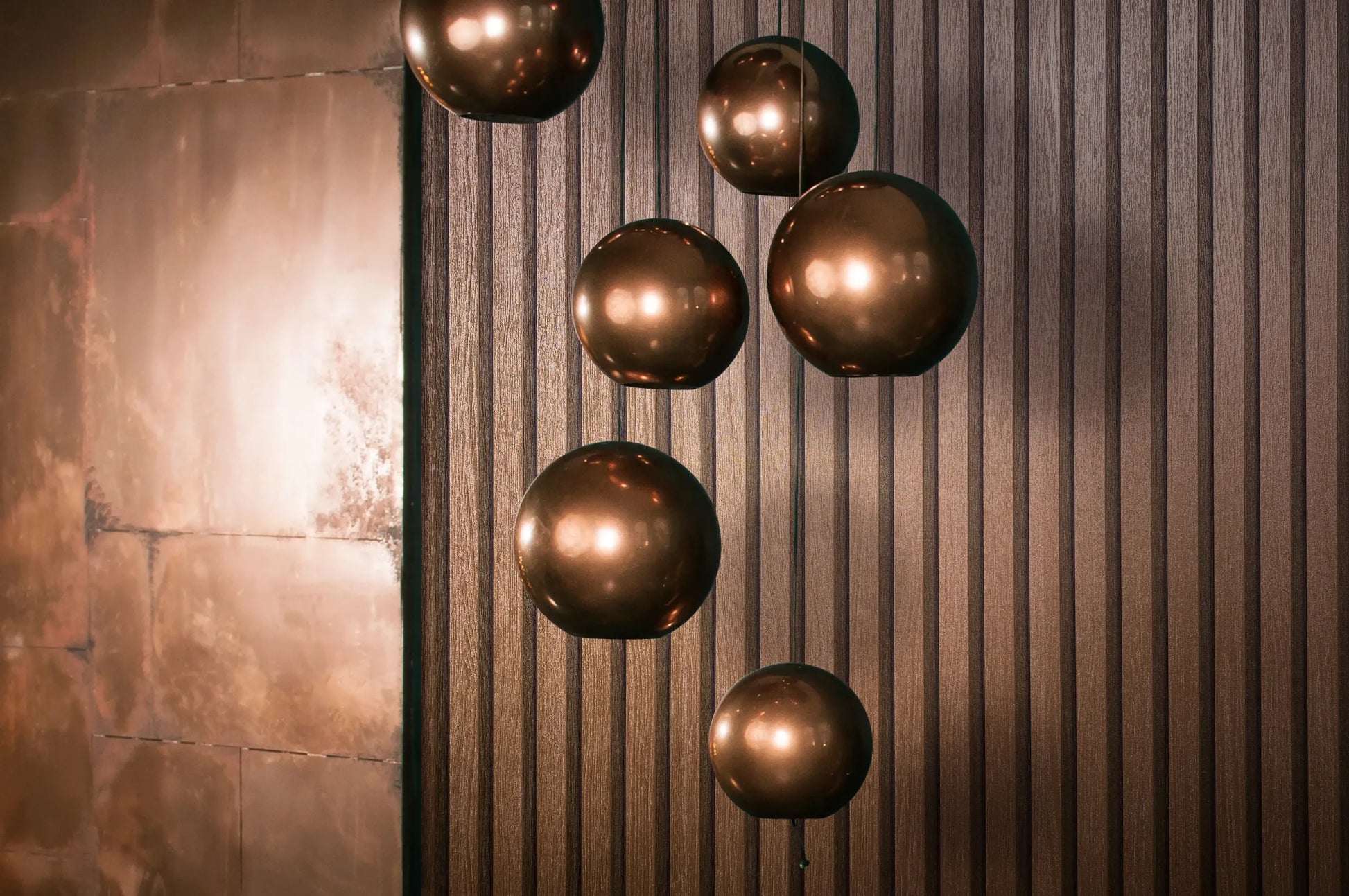 Marburg Travertino 33397 Metallic copper vertical-ribbed wallpaper with several glossy copper globe pendant lights in front and a metal wall panel on the left edge.